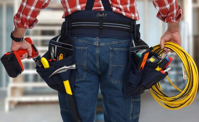 Electrician man with drill and wire cable over construction background.