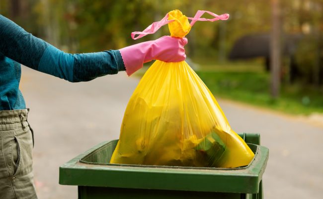 hand put a yellow plastic unsorted garbage bag into trash bin. household waste